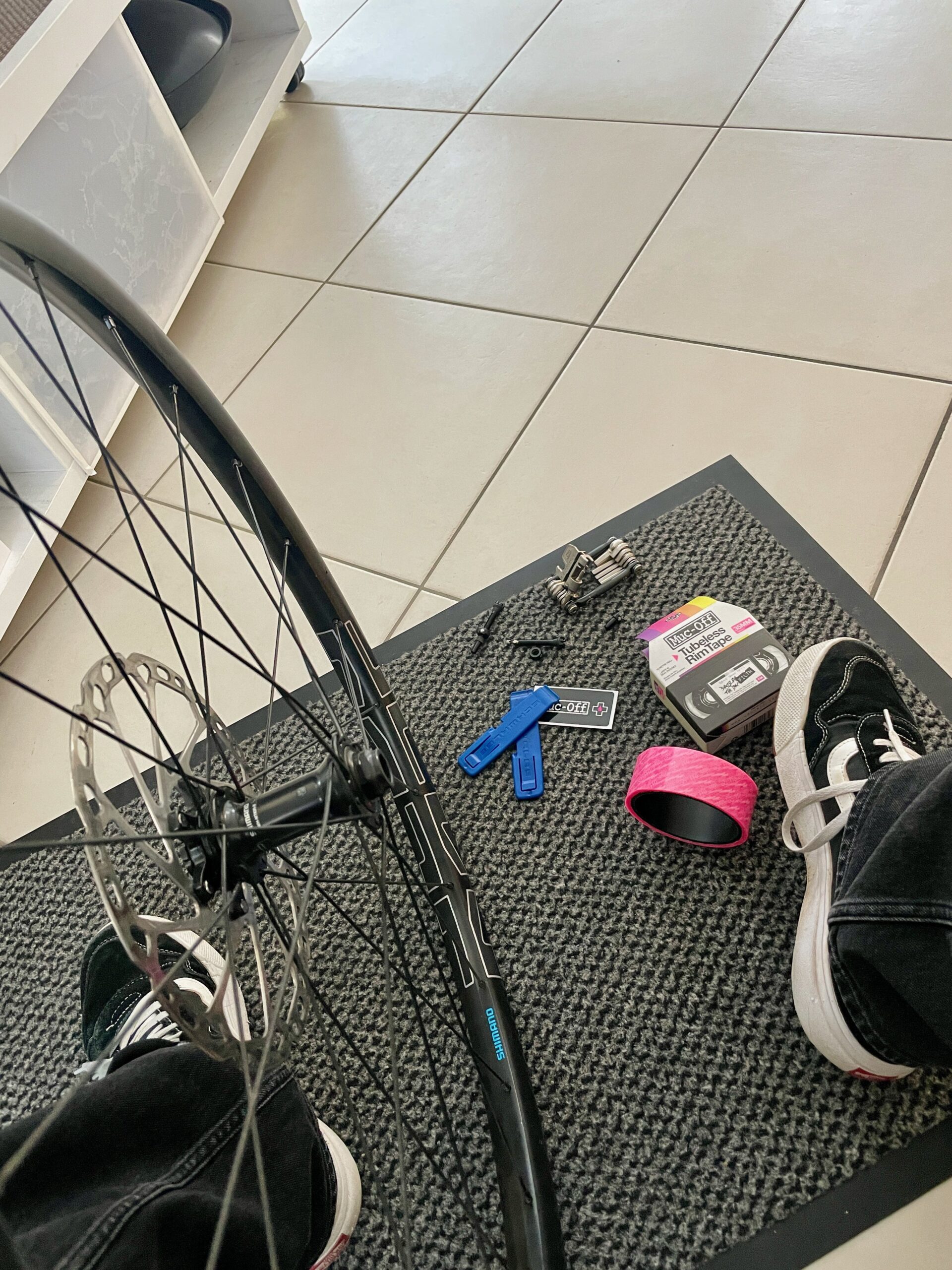 Auf einer Fußmatte ausgebreitet: Laufrad, Reifenheber, Tubeless-Ventile, Dichtmilch und Felgenband