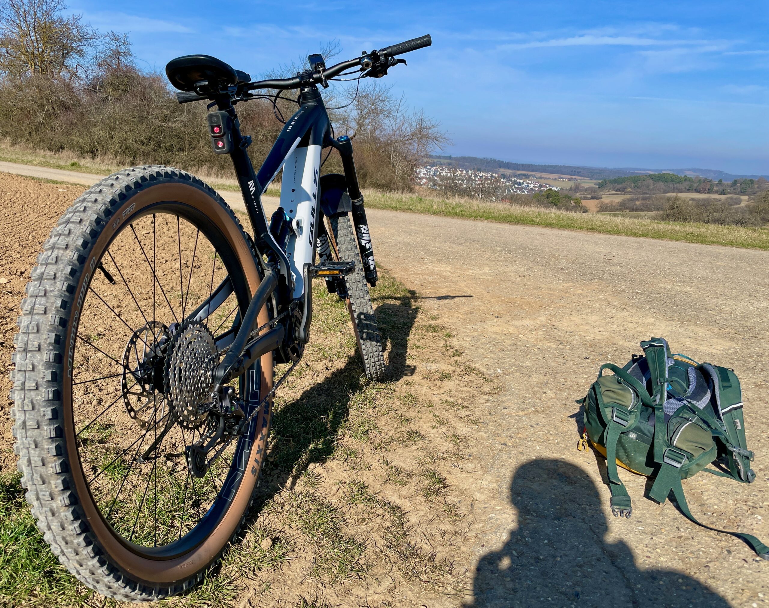 Mountainbike mit braunen Reifenflanken auf einem Schotterweg, im Hintergrund Felder